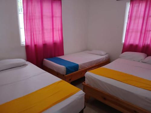 three beds in a room with pink and yellow curtains at Villa en Boca chica in Boca Chica