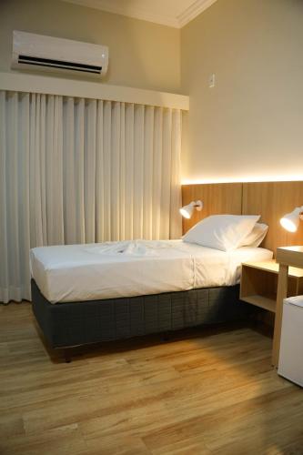 a bedroom with a bed with white sheets and a window at Gran Vale Hotel in Guanhães