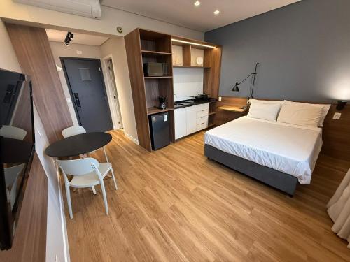 a bedroom with a bed and a table and a kitchen at Apto Studio novo, a passos da Praia com lazer completo in Santos