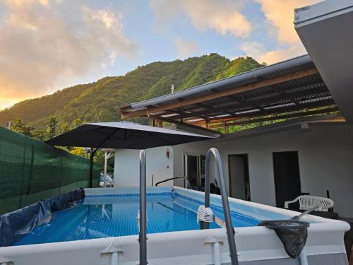 a swimming pool with an umbrella next to a house at Fare Tehaikinoa Teahupo'o in Teahupoo