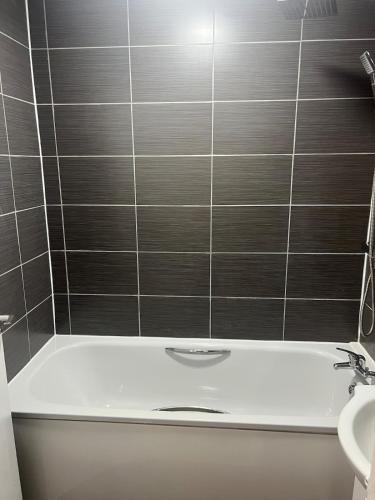 a bathroom with a bath tub with a tile wall at The Cosy Haven - 2 Bedroom house in Manchester