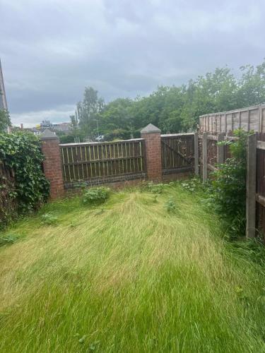 a fence with a field of tall grass next to a gate at The Cosy Haven - 2 Bedroom house in Manchester