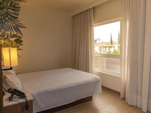 a bedroom with a white bed and a window at ibis Styles Curitiba Aeroporto in São José dos Pinhais