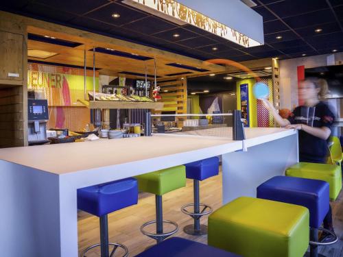 Una barra en un restaurante de comida rápida con taburetes coloridos. en ibis budget Reims Parc Des Expositions, en Reims