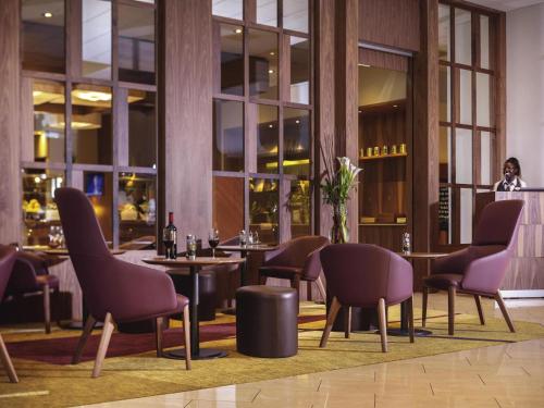 a restaurant with purple chairs and tables and a woman at Mövenpick Hotel Zürich-Regensdorf in Regensdorf