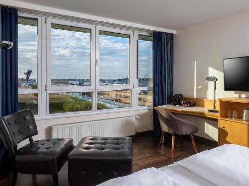 a hotel room with a bed and a desk and windows at Mövenpick Hotel Nürnberg Airport in Nürnberg