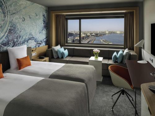 ein Hotelzimmer mit zwei Betten, einem Schreibtisch und einem Fenster in der Unterkunft Mövenpick Hotel Amsterdam City Centre in Amsterdam