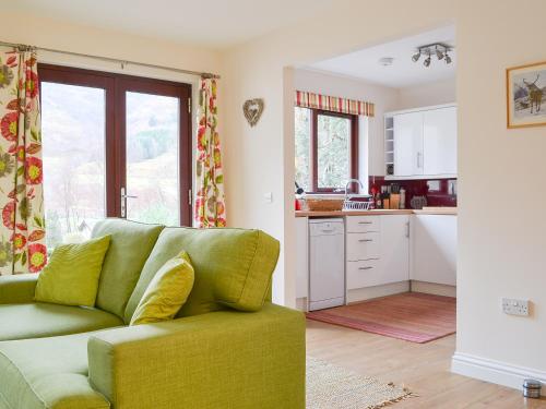 a living room with a green couch and a kitchen at Pine Marten Cottage in Ballachulish