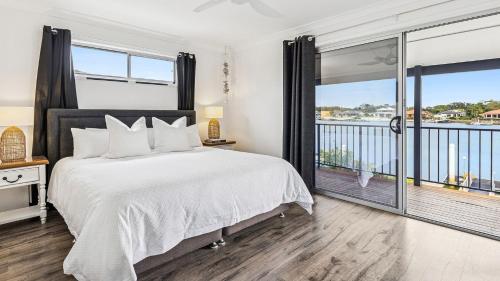 a bedroom with a large bed and a balcony at Pandanus - Spacious Waterfront Escape with Private Pontoon & Pool - Holiday Yamba in Yamba