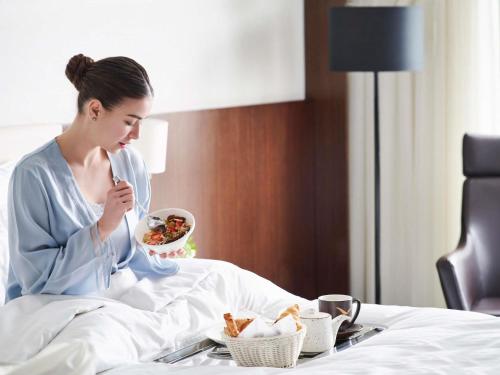 a woman sitting in a bed eating a bowl of food at Mövenpick Hotel Amman in Amman