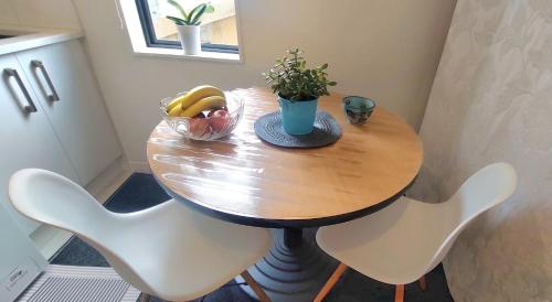 Una mesa de madera con dos sillas blancas y un bol de fruta. en Nature Escape Near Orewa Beach, en Silverdale