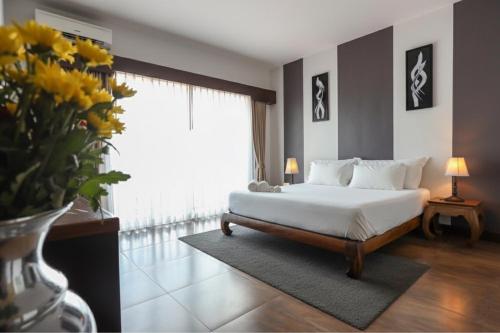 Un dormitorio con una cama y un jarrón de flores. en The Bridge Residence Hotel, en Kanchanaburi