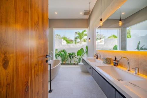 ein Badezimmer mit zwei Waschbecken, einer Badewanne und einem großen Fenster in der Unterkunft Luxury 4BR Villa Private Pool & Sea Horizon in Kerobokan
