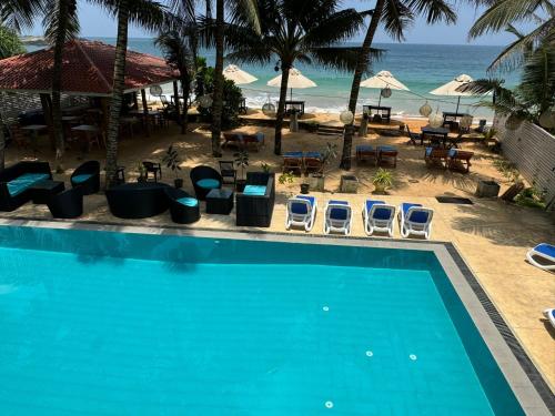una piscina con sillas y mesas y la playa en Nico Beach Hotel, en Hikkaduwa