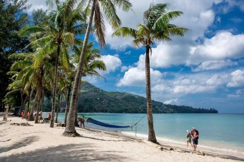 una pareja caminando por la playa con palmeras en The Escape Kamala, en Kamala Beach