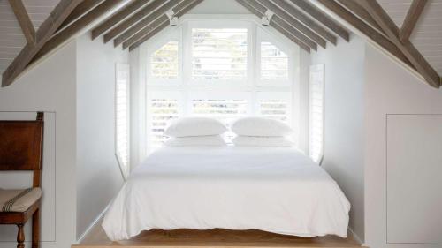 a bedroom with a white bed with a window at Kutti Beach House in Sydney