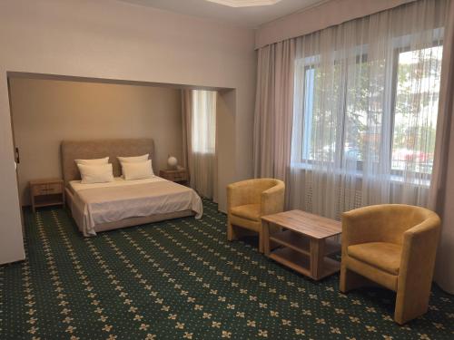 a hotel room with a bed and chairs and a window at Saya Hotel Almaty in Almaty