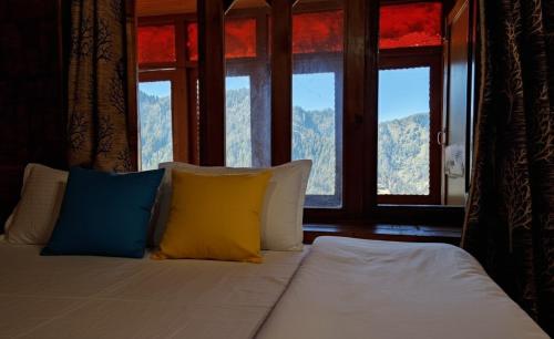 a bed with yellow and blue pillows in a room with windows at Oran Stays Shoja in Shoja