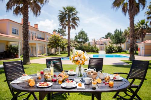 a table with food on it in a yard with palm trees at The Village – Praia D’El Rey Golf & Beach Resort in Casal da Lagoa Seca