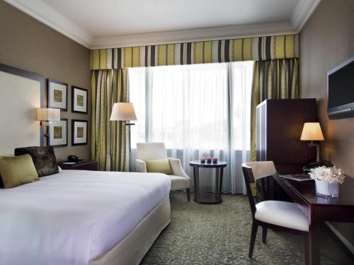 a hotel room with a bed and a desk and a window at Mövenpick Grand Al Bustan in Dubai