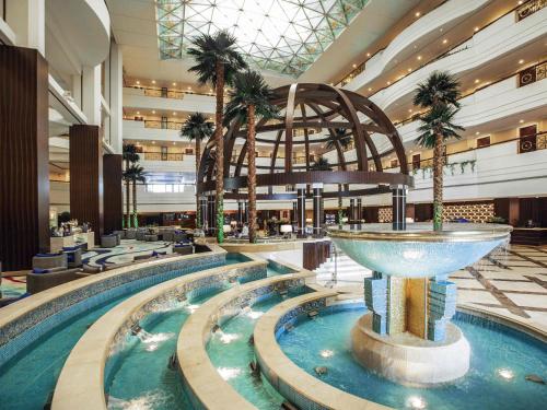 a large pool with a fountain in a hotel lobby at Mövenpick Grand Al Bustan in Dubai