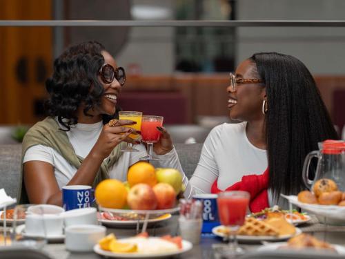 dos mujeres sentadas en una mesa con comida y bebidas en Novotel Kinshasa La Gombe, en Kinshasa