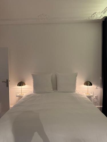 a white bed with white pillows and two lamps at La suite du parc 1 in Nancy