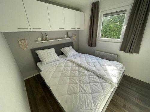 a bedroom with a white bed with a window at Chalet 130 in Petten