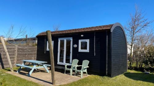 a black tiny house with two chairs and a picnic table at Campervan in Petten