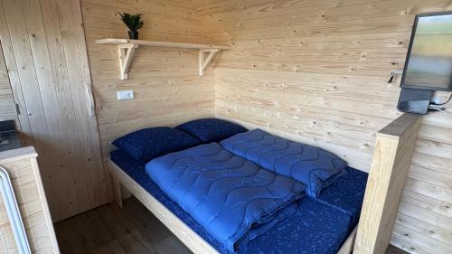 a blue bed in a wooden room with a tv at Kampeerwagon in Petten