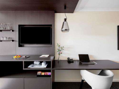a room with a desk with a laptop and a tv at Mantra on Northbourne in Canberra