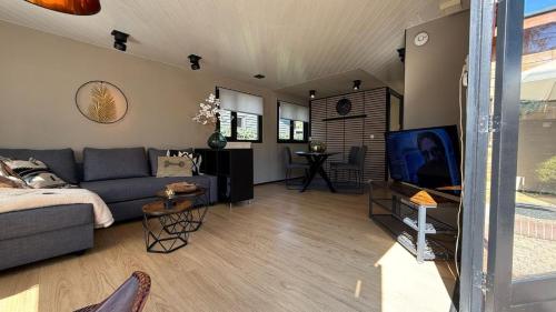 a living room with a couch and a tv at VELUWE VOORTHUIZEN COMFORTABLE CHALET - Comfortable Chalet with Good Amenities and several Activities for Families and Tourists nearby in Voorthuizen
