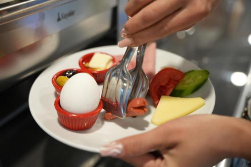 una persona che tiene una forchetta e un piatto con uova e verdure di Kent Room Hotel a Kapaklı