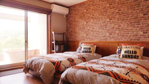 zwei Betten in einem Zimmer mit einer Ziegelwand in der Unterkunft KOKOPELLI HOUSE IZUKOGEN -Private Hot Spring- in Ito