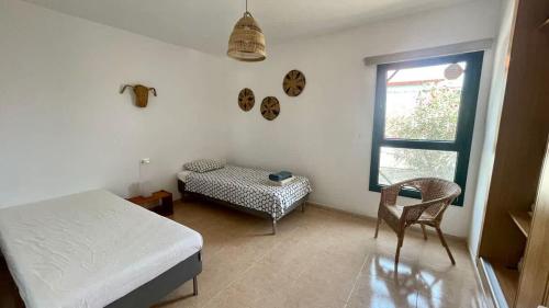 Un dormitorio con una cama y una silla y una ventana. en Villa spacieuse et lumineuse avec piscine Chauffée, en La Oliva