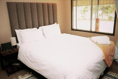 Un dormitorio con una gran cama blanca con ventana. en EastClaire Guesthouse, en Krugersdorp