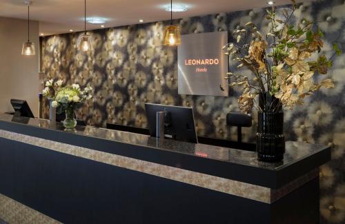 a lobby with a reception desk with flowers on the wall at Leonardo Hotel Hamburg City Nord in Hamburg