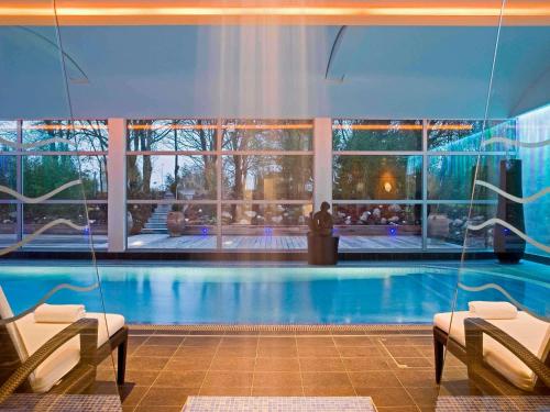 a large swimming pool with two chairs in a building at Mercure Paris CDG Airport & Convention in Roissy-en-France