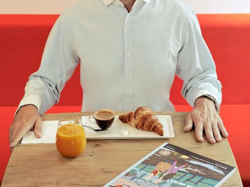 een man aan een tafel met een bord koffie en croissants bij ibis Montélimar Nord in Saulce-sur-Rhône