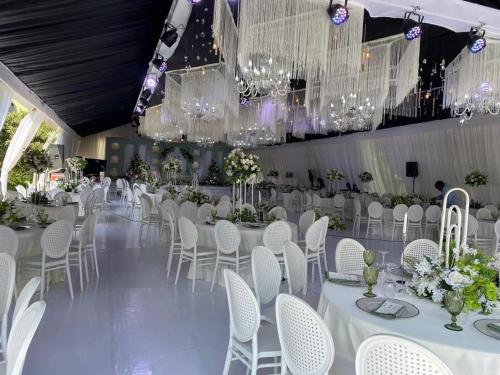 une salle de banquet avec des tables blanches, des chaises et des lustres dans l'établissement ARCH APARTMENTS and HOTEL, à Kampala