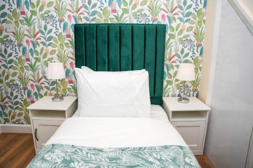 a bed with a green headboard next to two night stands at Spacious 4-Bed Home with Free Parking in Heston