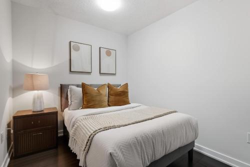 a white bedroom with a bed with pillows and a lamp at Trendy 1BR Condo Free Parking Downtown Toronto in Toronto