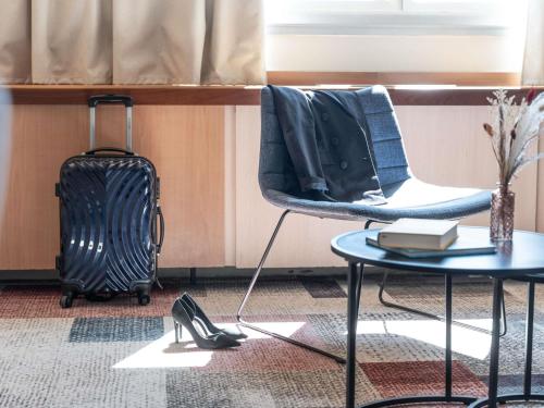una habitación con una silla y una mesa y una maleta en Mercure Besancon Parc Micaud - Hotel & Bar, en Besançon