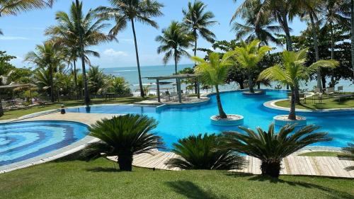 a large swimming pool with palm trees and the ocean at Bahia Outeiro das Brisas - Gibs' House in Porto Seguro