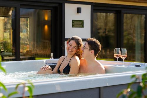 2 personnes assises dans une baignoire avec verres à vin dans l'établissement Woodz Lodges - Unwind in nature, à Bolderberg