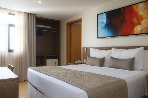 a hotel room with a large white bed with a tv on the wall at Vida Plaza Hotel in Brasília