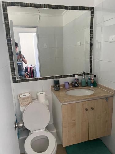 a man taking a picture of a bathroom with a toilet and sink at Cómodo departamento in El Tabo