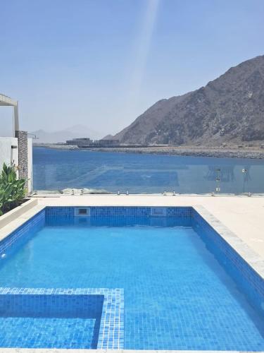 a large blue swimming pool next to a body of water at Al Dana Sea Luxury Villa Fujairah in Sharm