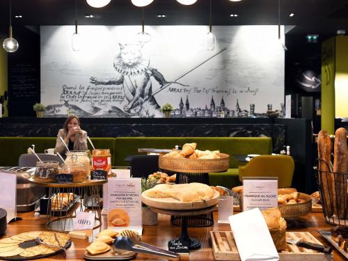Eine Frau sitzt an einem Tisch mit Brot und Gebäck. in der Unterkunft Mercure Arras Centre Gare in Arras