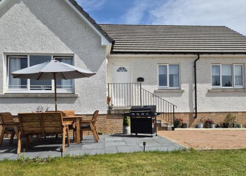 a table and chairs with an umbrella in front of a house at Kilin in Lochgilphead